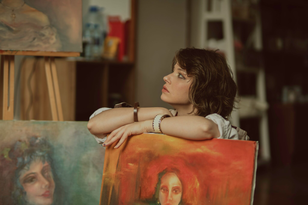 Eine Frau betrachtet nachdenklich ihre eigenen Bilder in einem Atelier