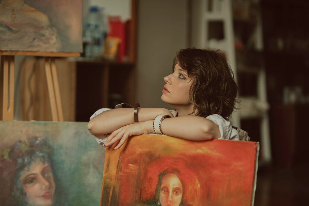 Frau betrachtet nachdenklich ihr selbst gemaltes Bild in einer kunsttherapeutischen Umgebung.
