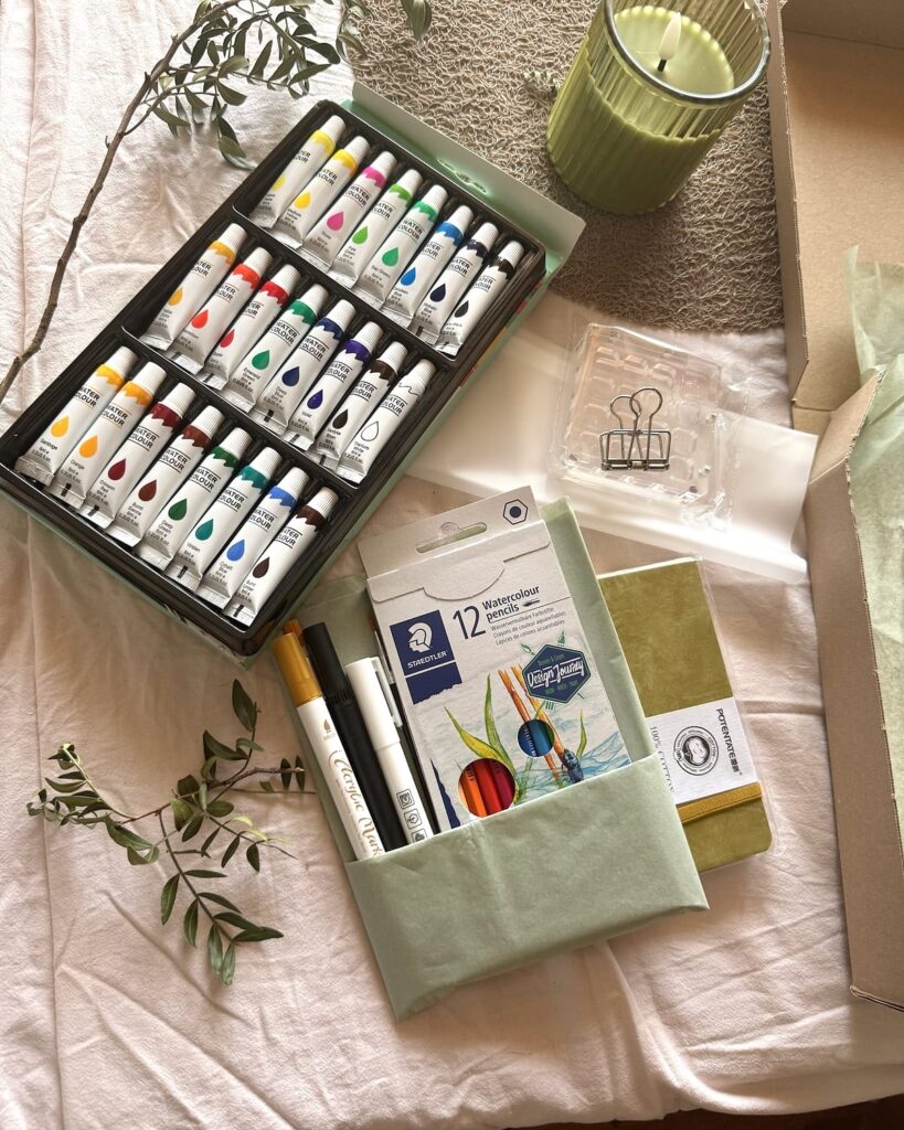 Aquarellfarben, Stifte und Papier der KreativBox „Mein Wohlfühlort“ mit natürlichen Zweigen dekoriert